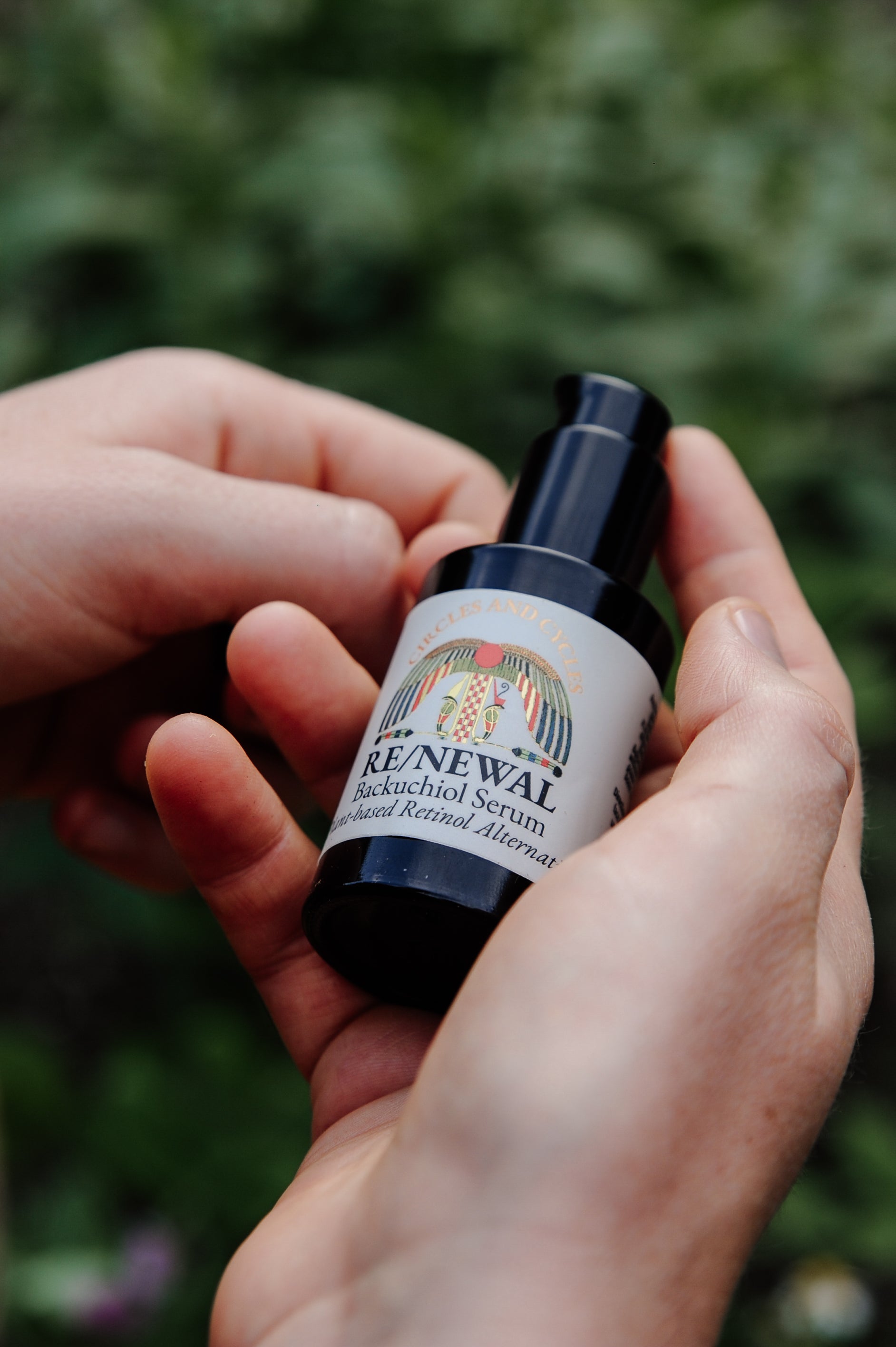 Bottle of 'Renewal' serum held in a hand with a blurred green background