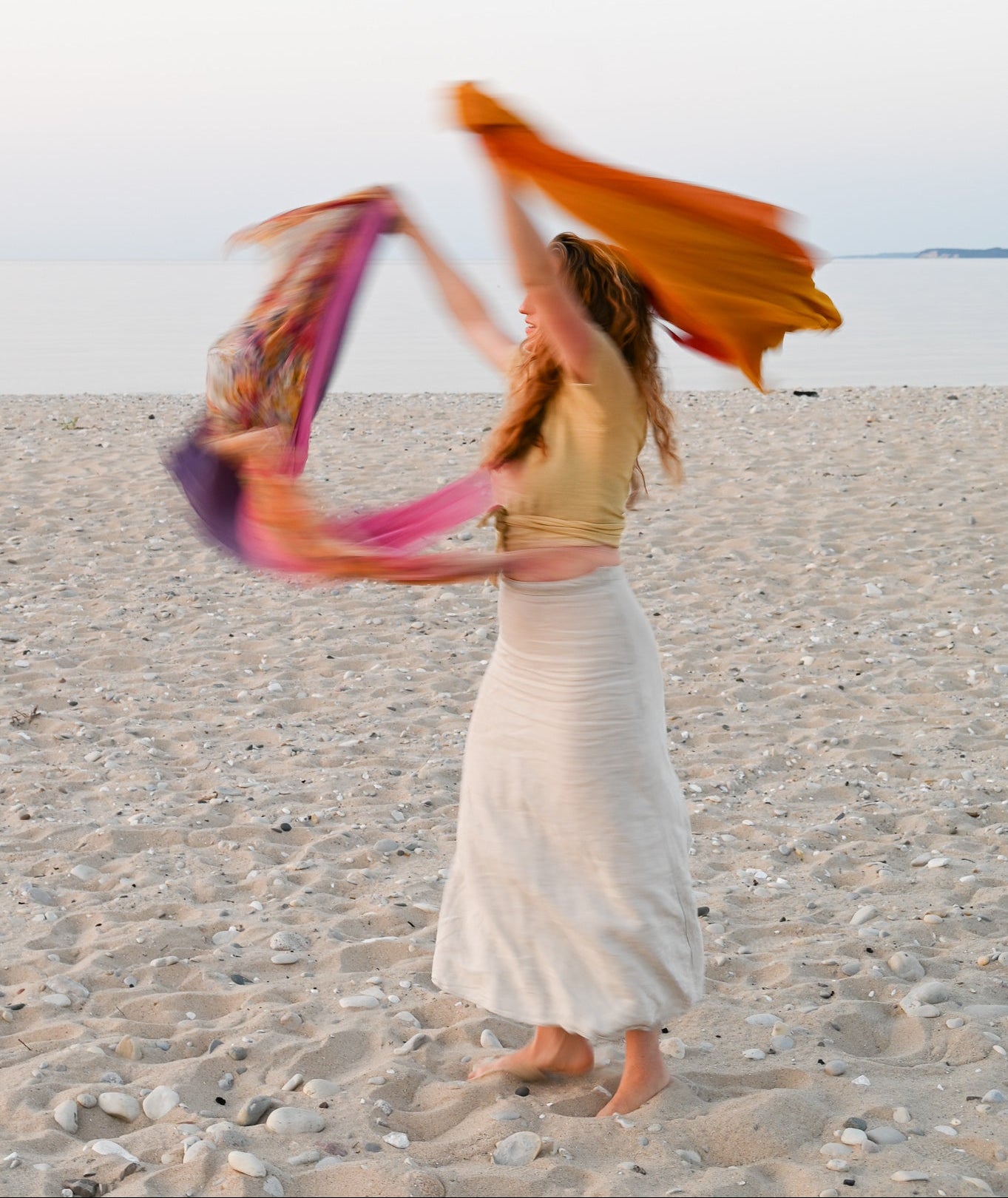 Woman twirling on a beach with colorful scarves.