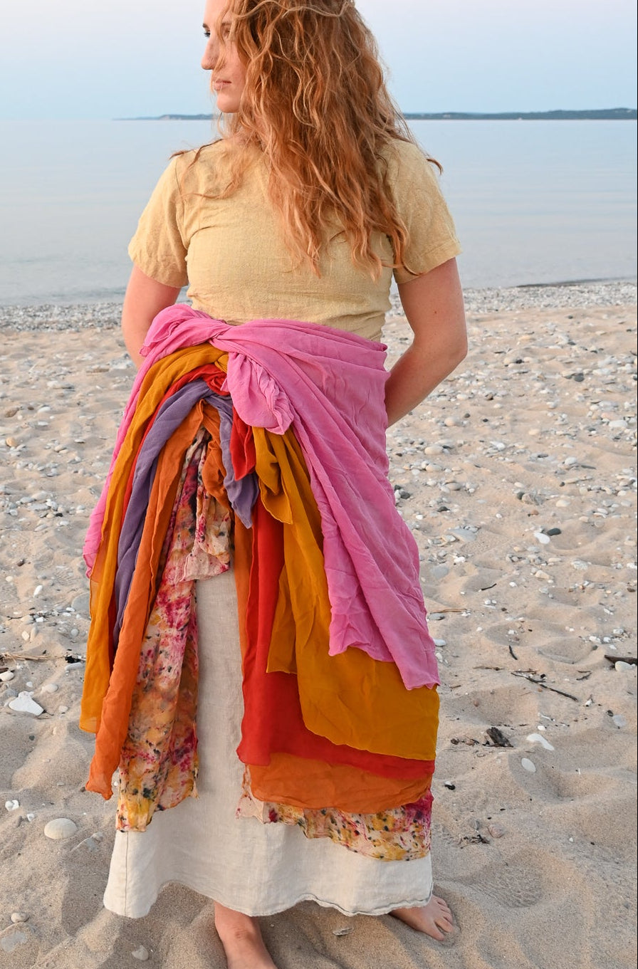 Woman standing on a beach with several colorful scarves wrapped around her waist