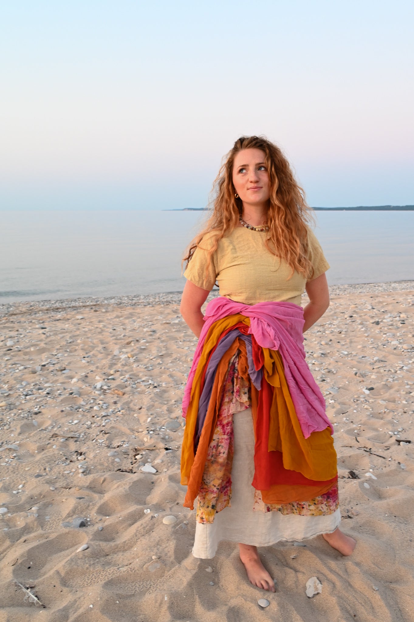 Woman standing on a beach with colorful scarves wrapped around her waist