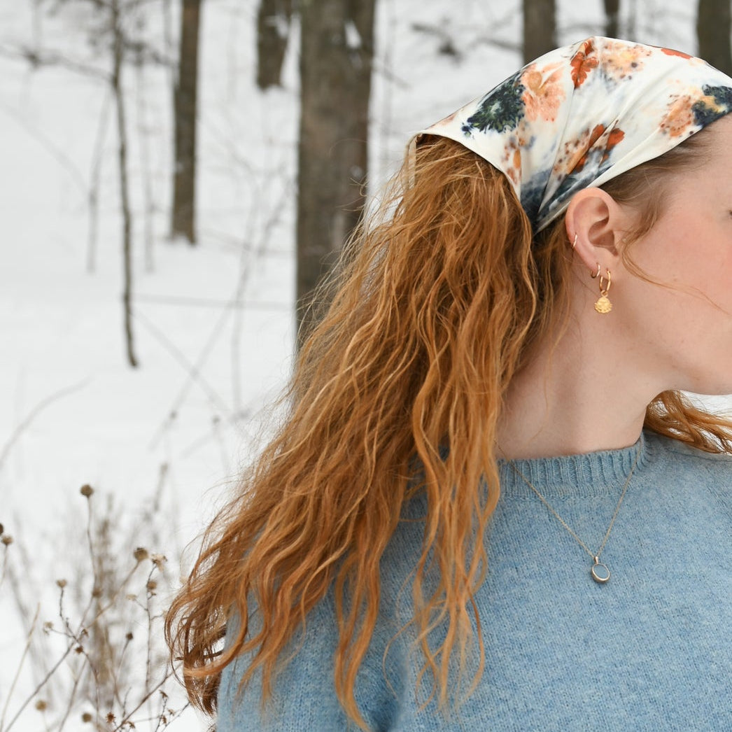 Person wearing a blue sweater and floral bandana in a snowy forest