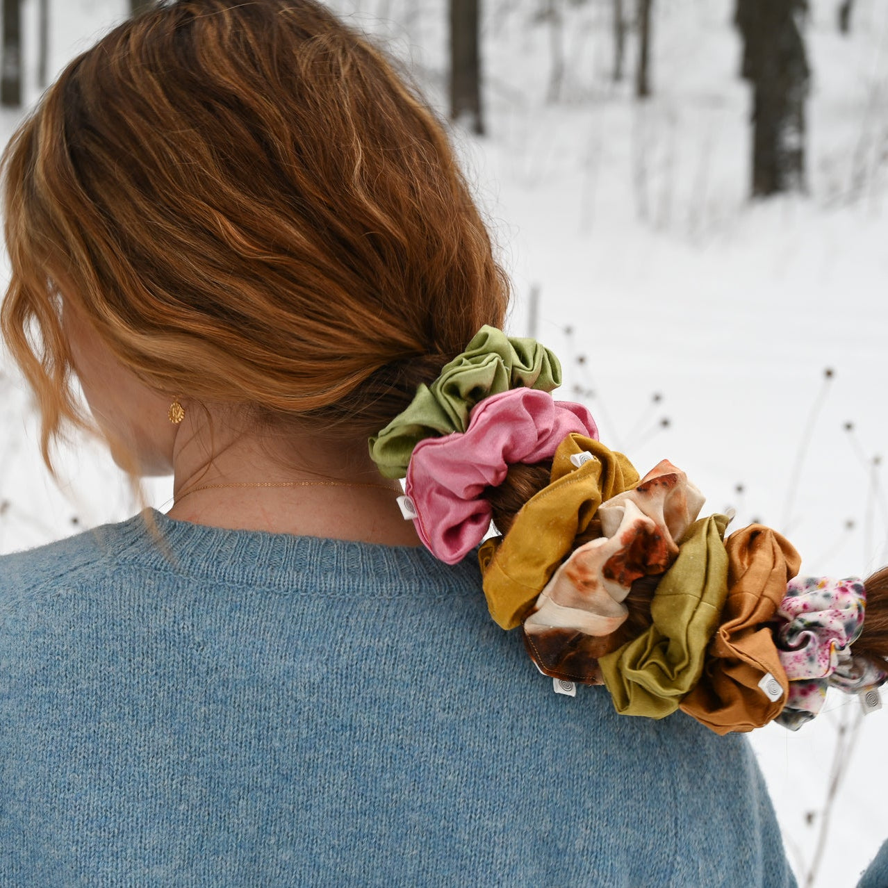 Person with colorful scrunchies in a bun against a snowy forest background