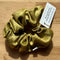 Gold scrunchie with a label on a wooden surface