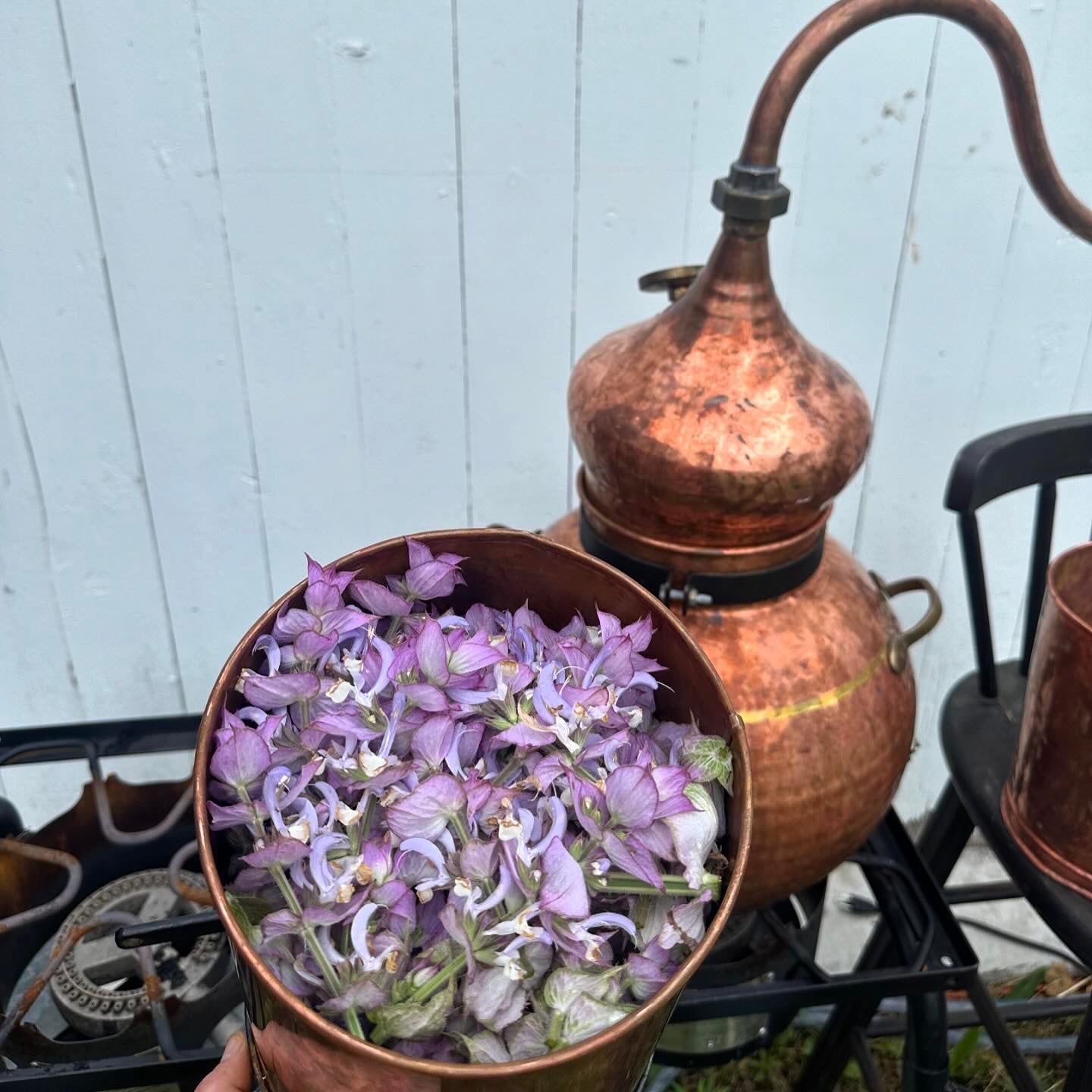 Copper still with flowers inside against a white wooden panel background