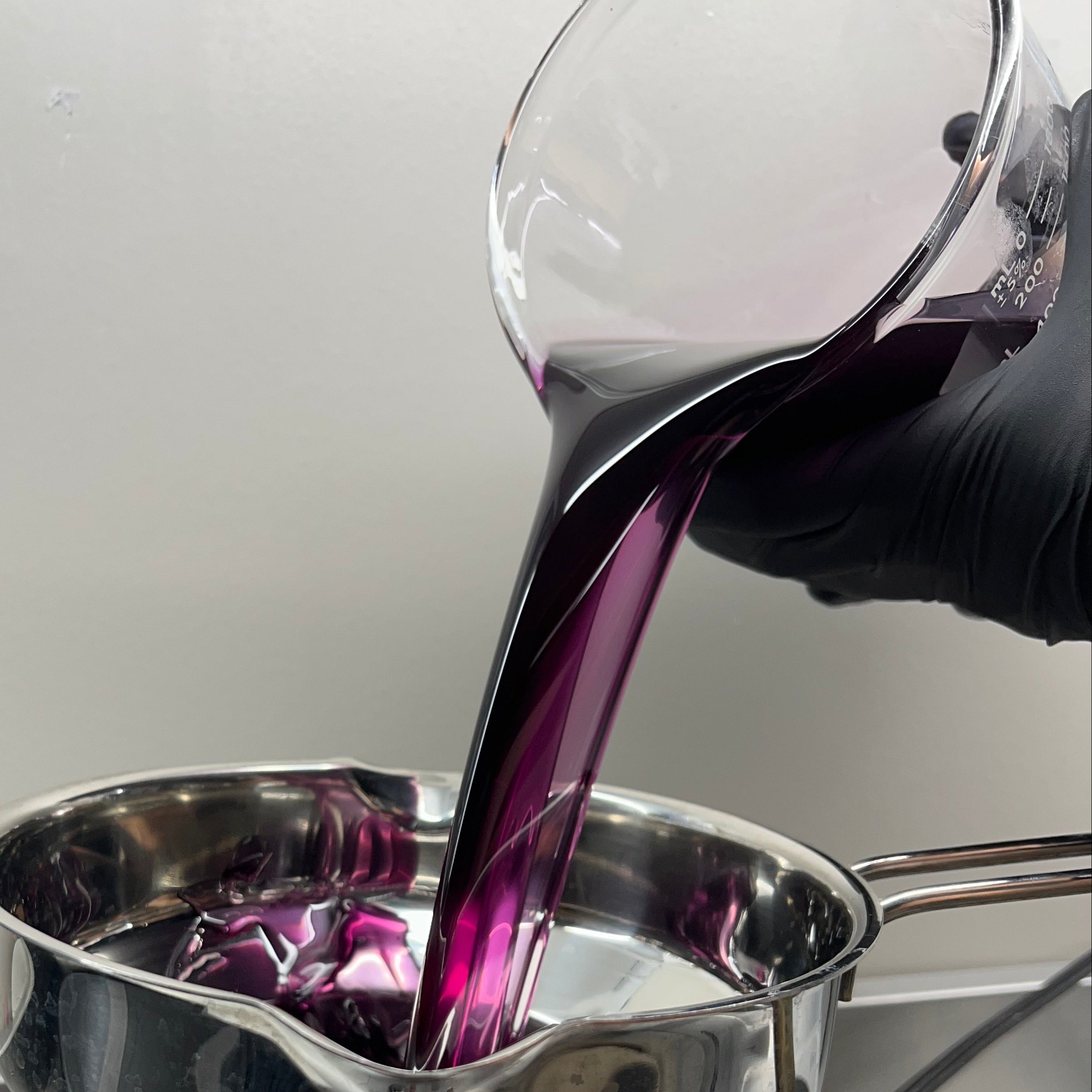 Copper pot with a purple liquid being poured into it, on a white background.