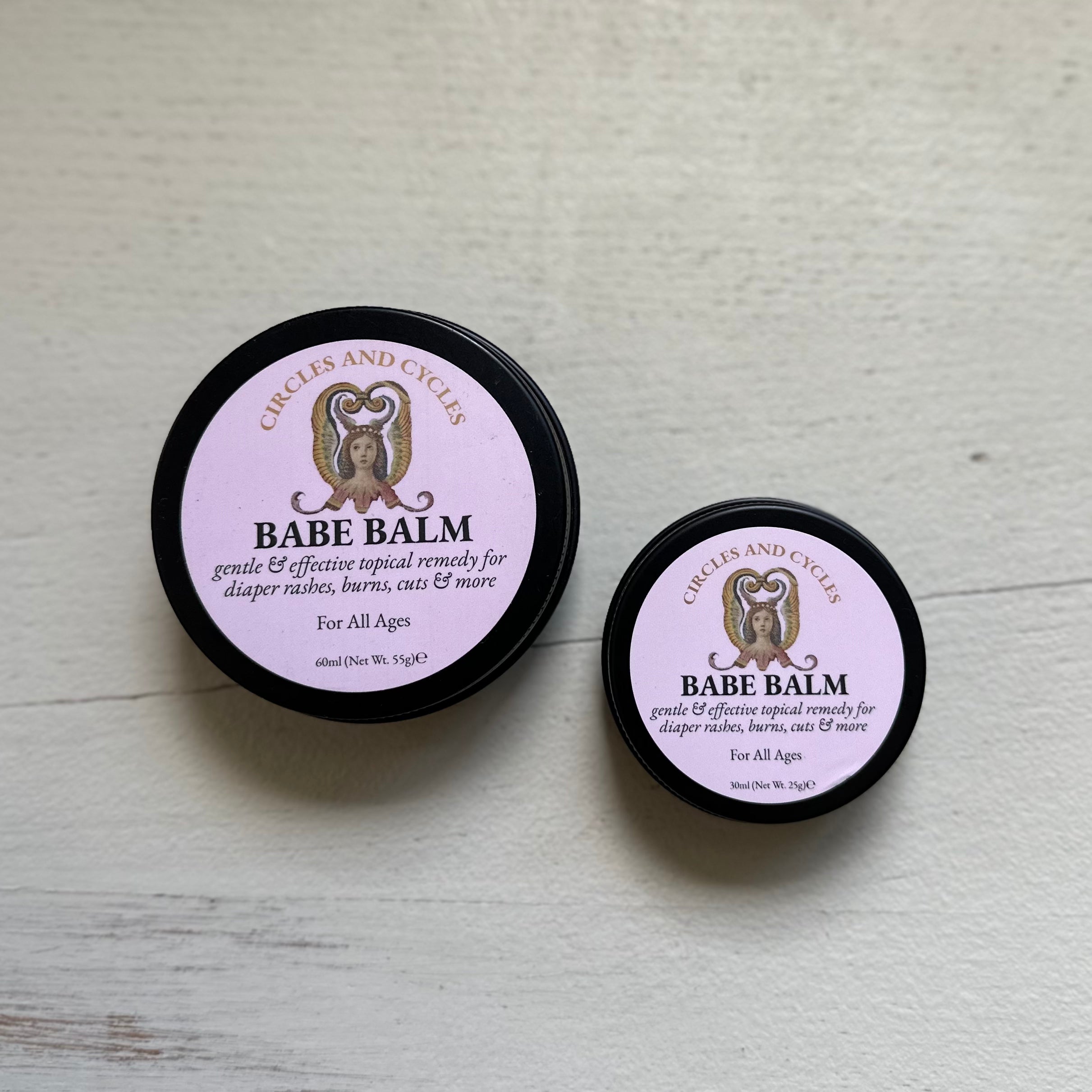 Two containers of Babe Balm on a light wooden surface