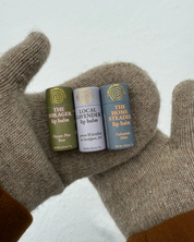 Three lip balm tubes held in a gloved hand against a light background