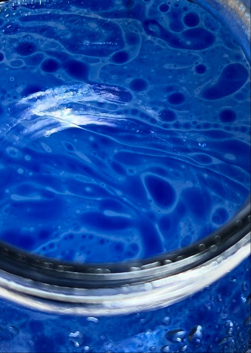 Close-up of a jar with blue oil and liquid swirling together